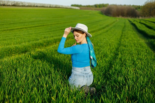 Jeune femme séduisante en chapeau blanc chemise bleue jean bleu posant dans un champ vert d'été Copier l'espace vide pour le texte