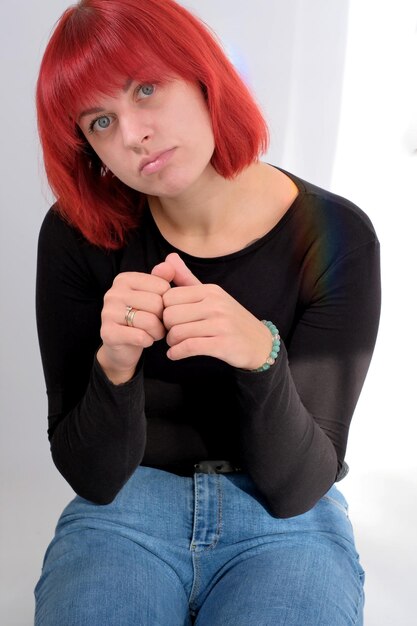 Une jeune femme séduisante avec une coiffure courte orange dans un T-shirt noir et un jean posant en studio sur fond blanc