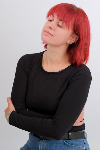 Une jeune femme séduisante avec une coiffure courte orange dans un T-shirt noir et un jean posant en studio sur fond blanc