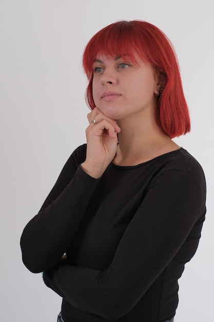 Une jeune femme séduisante avec une coiffure courte orange dans un T-shirt noir et un jean posant en studio sur fond blanc