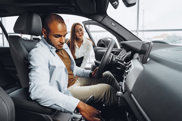 Jeune femme séduisante dans la salle d'exposition de voiture montrant une voiture à son client masculin