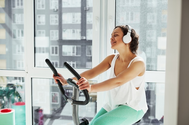 Jeune femme séduisante écouter de la musique tout en travaillant sur spin bike