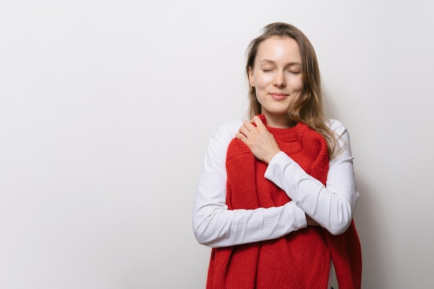 Jeune femme séduisante étreint rêveusement son pull rouge tout en choisissant des vêtements sur fond blanc isolé Place pour votre conception