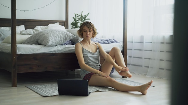 Jeune femme séduisante faisant de l'exercice de yoga et regardant une leçon de tutoriel sur un ordinateur portable à la maison