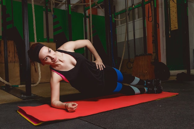 Jeune femme séduisante fait des exercices de planches tout en travaillant dans un gymnase