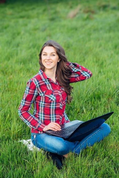 Jeune femme séduisante avec un ordinateur portable sur l'herbe dans un jardin fleuri