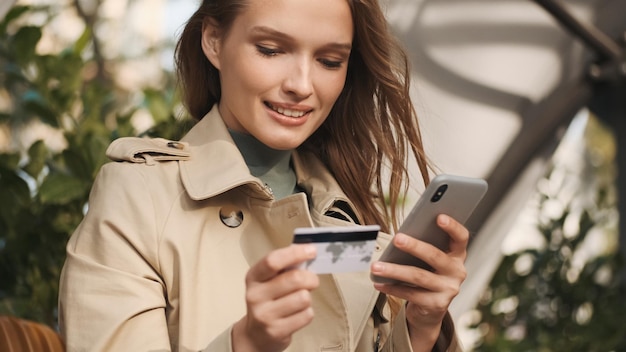 Jeune femme séduisante payant des achats en ligne par carte de crédit à l'aide d'un smartphone lors d'une pause-café dans un café en plein air