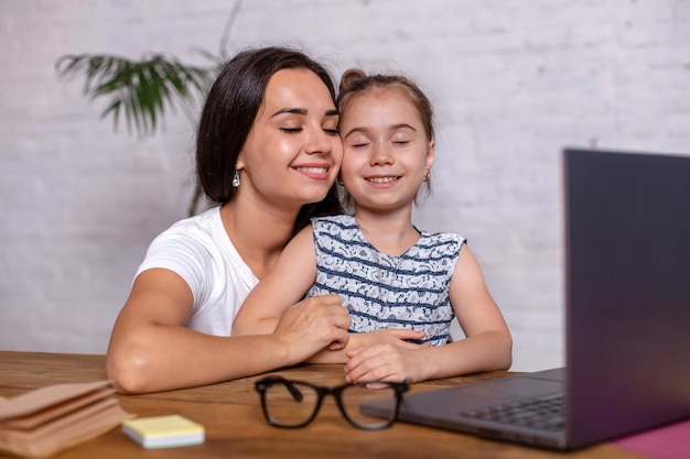 Une jeune femme séduisante et sa petite fille mignonne sont assises à la table et s'amusent tout en faisant leurs devoirs ensemble. La mère aide sa fille avec ses cours à l'école.