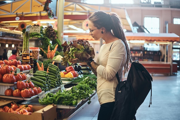 Photo jeune femme séduisante avec des tatouages choisissant une salade fraîche au marché aux légumes.