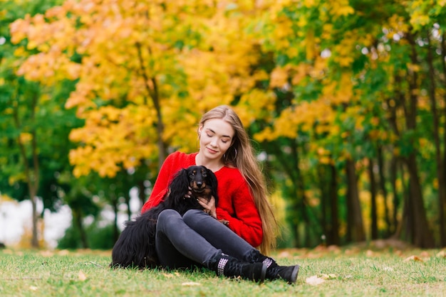 Jeune femme séduisante tenant son chien teckel dans ses bras à l'extérieur au lever du soleil dans le parc à l'automne