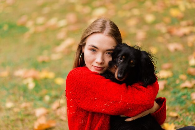 Jeune femme séduisante tenant son chien teckel dans ses bras à l'extérieur au lever du soleil dans le parc à l'automne