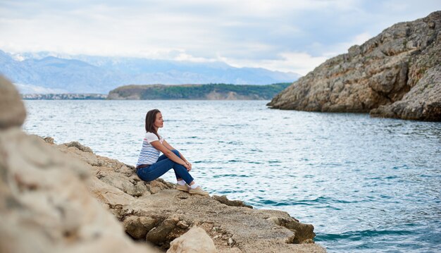 Jeune femme séduisante touriste assis seul sur le rivage pierreux de la mer, bénéficiant d'une belle vue