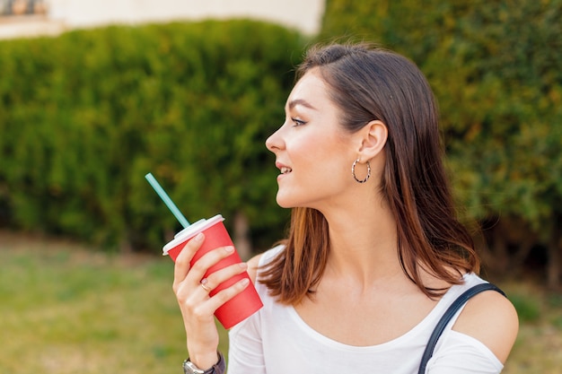 Jeune femme séduisante avec un verre dans une rue par une journée ensoleillée