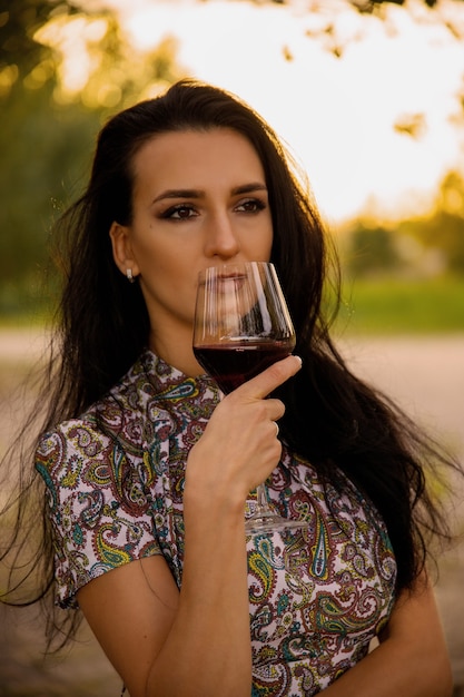 Jeune femme séduisante avec un verre de vin rouge sur la nature