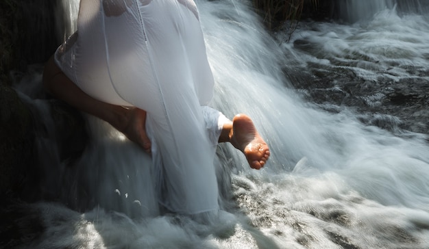 Une jeune femme semi-nue en robe blanche apprécie la fraîcheur et la fraîcheur des jets d'eau de la cascade