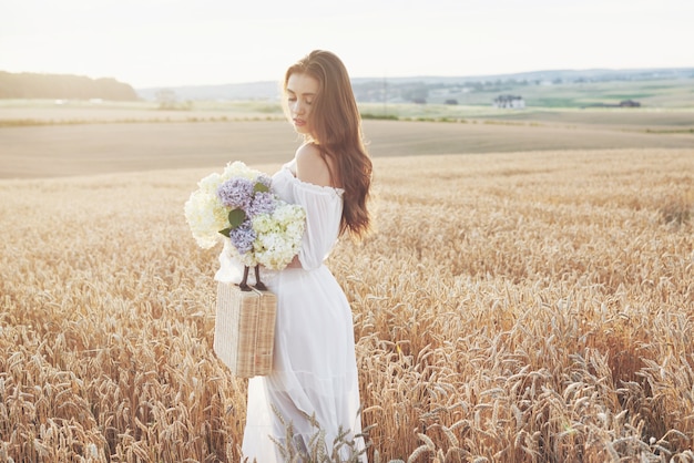 Jeune femme sensible en robe blanche posant dans un champ de blé doré