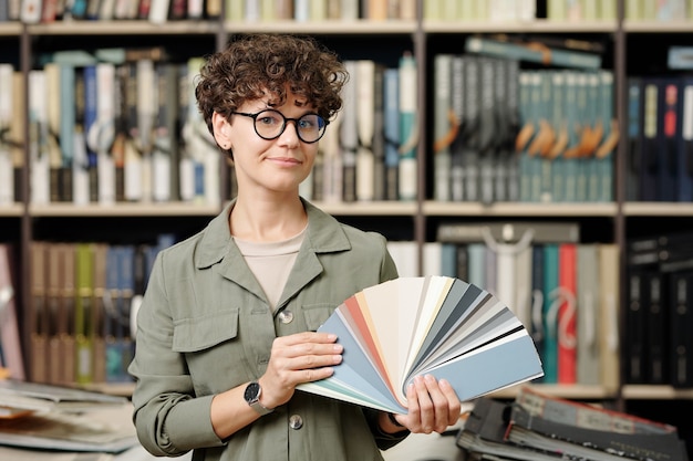 Jeune femme sérieuse directrice d'un studio de design d'intérieur qui vous regarde tout en montrant une palette avec des échantillons de cuir neuf pour meubles