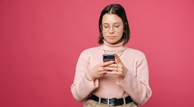 Une jeune femme sérieuse envoie des SMS au téléphone sur fond rose