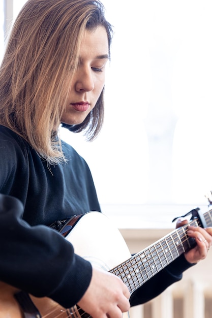 Jeune femme sérieuse jouant de la guitare acoustique à la maison