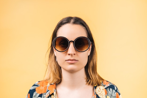 Jeune femme sérieuse portant une chemise fleurie et de grandes lunettes de soleil rondes