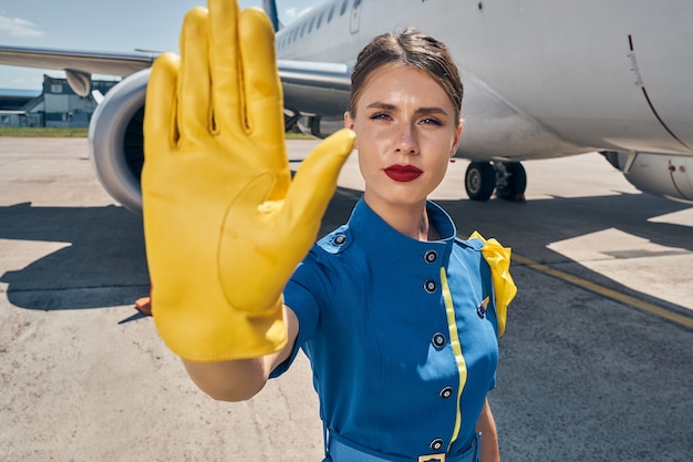 Jeune femme sérieuse en uniforme tenant une main gantée surélevée devant la caméra