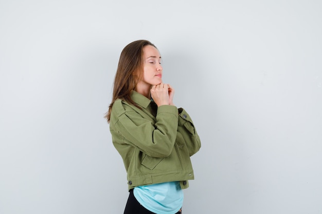 Jeune femme serrant les mains sous le menton dans un geste de prière en t-shirt, veste et l'air paisible. vue de face.