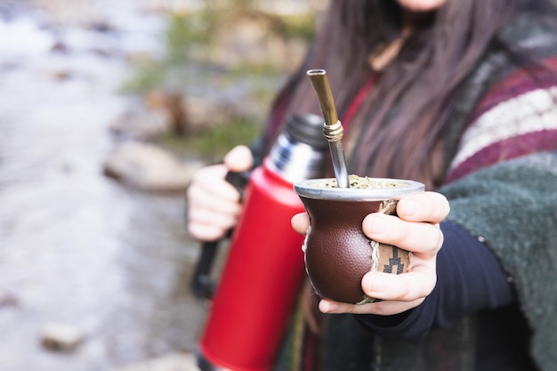 Jeune femme servant mate dans un espace naturel à côté d'une rivière boisson latine