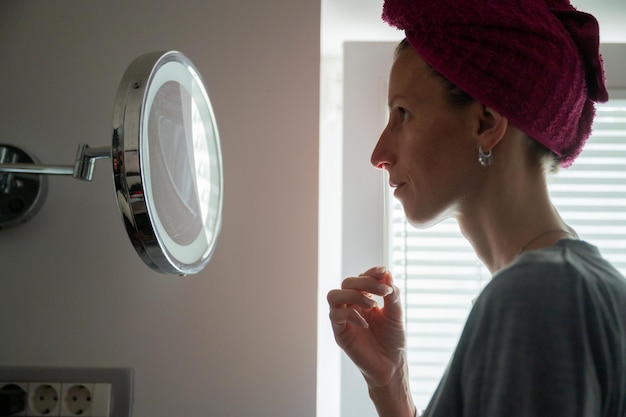 Jeune femme avec une serviette roulée sur ses cheveux mouillés prenant un écouvillon nasal à la maison pour tester le coronavirus dans une image conceptuelle de la pandémie mondiale et de la quarantaine