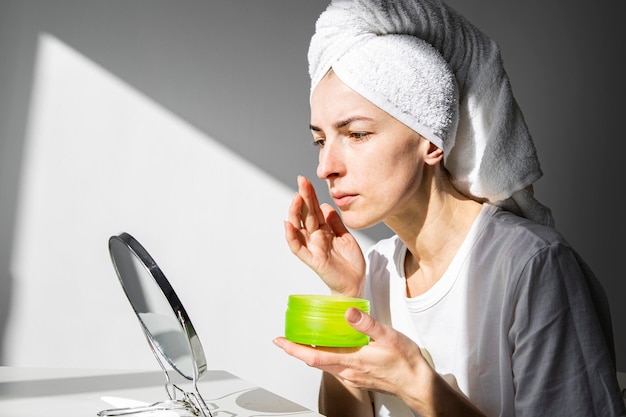 Jeune femme avec une serviette sur la tête en appliquant le maquillage du matin