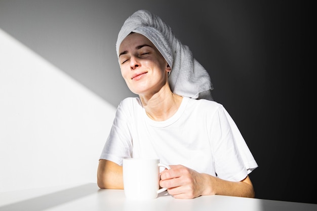 Jeune femme avec une serviette sur la tête en appréciant son café du matin