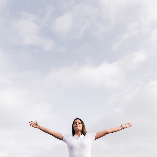 Photo jeune femme avec ses yeux fermés tendant ses mains contre le ciel bleu