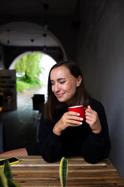 Une jeune femme seule à boire un verre dans un café de terrasse un jour de pluie