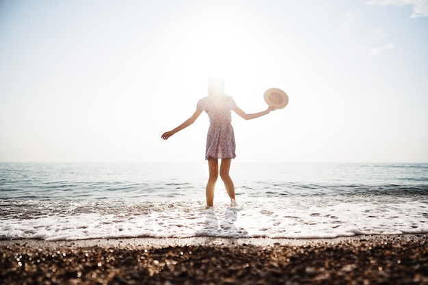 La jeune femme seule marche sur le bord de mer au coucher du soleil