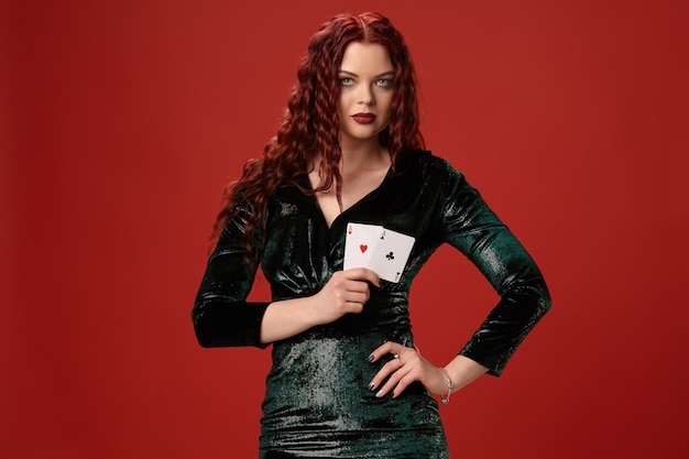 Jeune femme sexy avec des cheveux bouclés rouges tenant des as, sur fond rouge. Poker