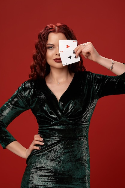 Jeune femme sexy avec des cheveux bouclés rouges tenant des as, sur fond rouge. Poker