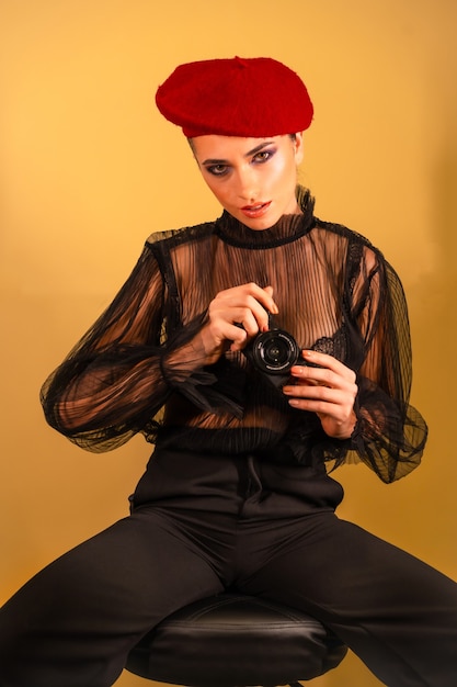 Une jeune femme sexy dans un béret rouge et une chemise transparente noire tenant la caméra