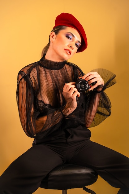 Une jeune femme sexy dans un béret rouge et une chemise transparente noire tenant la caméra