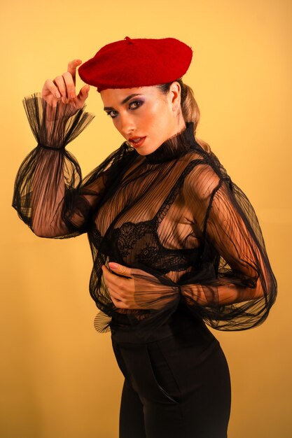 Une jeune femme sexy dans un chapeau de béret rouge et une chemise transparente noire posant