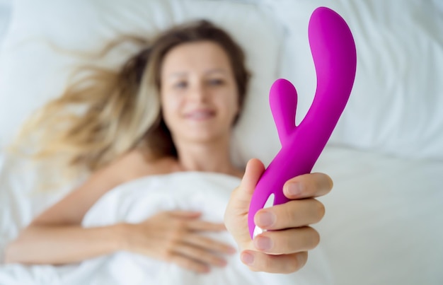 Jeune femme sexy dans le lit tenant dans ses mains un jouet sexuel pour adultes