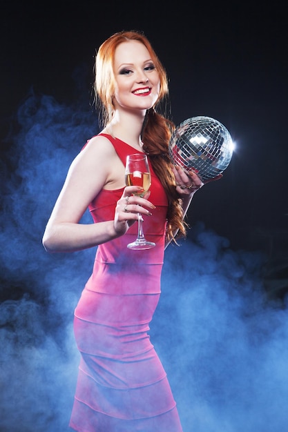 Jeune femme sexy en dres rouge gardant une boule disco sur fond sombre