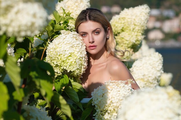 Jeune femme sexy ou une fille dans un buisson fleuri de fleurs d'hortensia sur fond naturel dans le jardin Grandes fleurs d'arbustes d'hortensias blancs