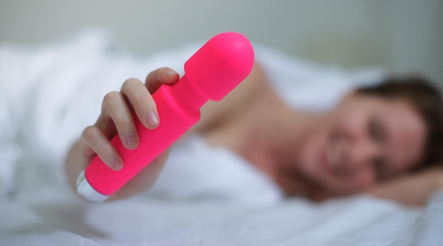 Jeune femme sexy heureuse tenir dans la main sex toy se masturber avec vibrateur au lit dans la chambre à la maison