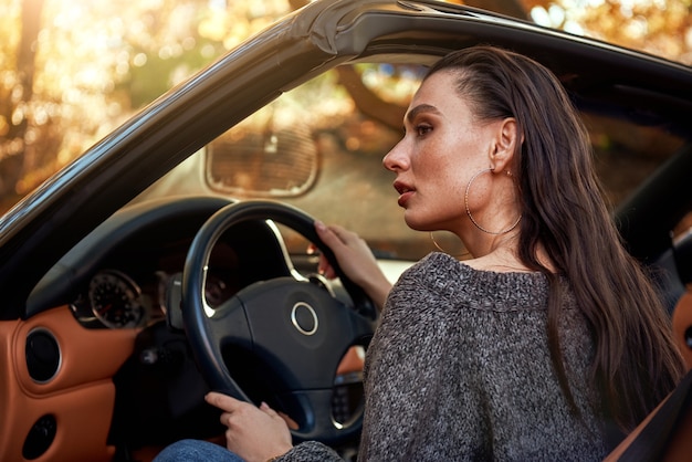 Une jeune femme sexy en jeans et en pull gris est assise dans un cabriolet