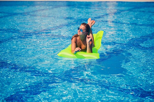 Jeune femme sexy en maillot de bain nage dans la piscine sur un matelas gonflable Fille à lunettes de soleil dans une piscine bleue en vacances