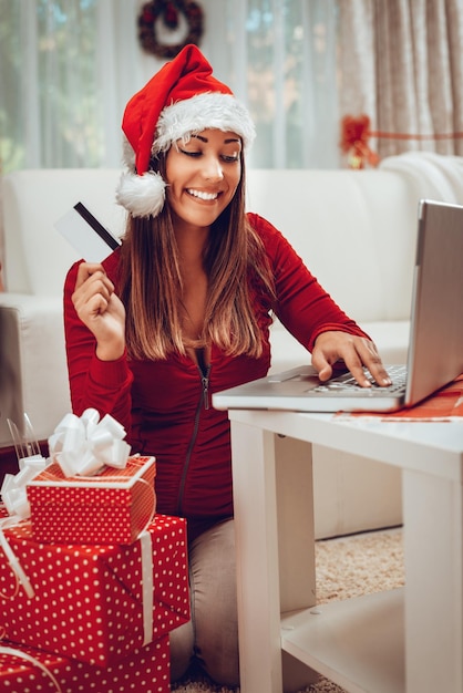 Jeune femme shopping en ligne avec carte de crédit à la maison pour Noël.