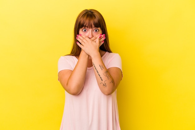 Jeune femme sinueuse caucasienne isolée sur fond jaune choqué couvrant la bouche avec les mains.