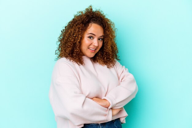 Jeune femme sinueuse latine isolée sur fond bleu en riant et en s'amusant.