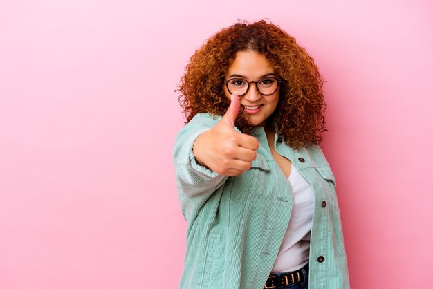 Jeune femme sinueuse latine isolée sur fond rose souriant et levant le pouce vers le haut