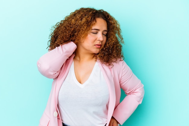 Jeune femme sinueuse latine isolée sur un mur bleu ayant une douleur au cou due au stress, en massant et en la touchant avec la main.