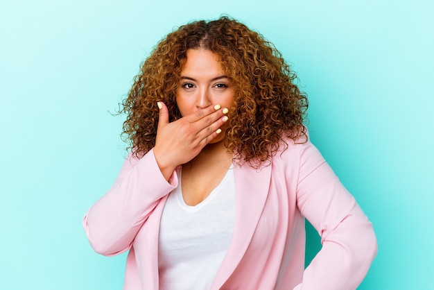 Jeune femme sinueuse latine isolée sur un mur bleu couvrant la bouche avec les mains à la peur.